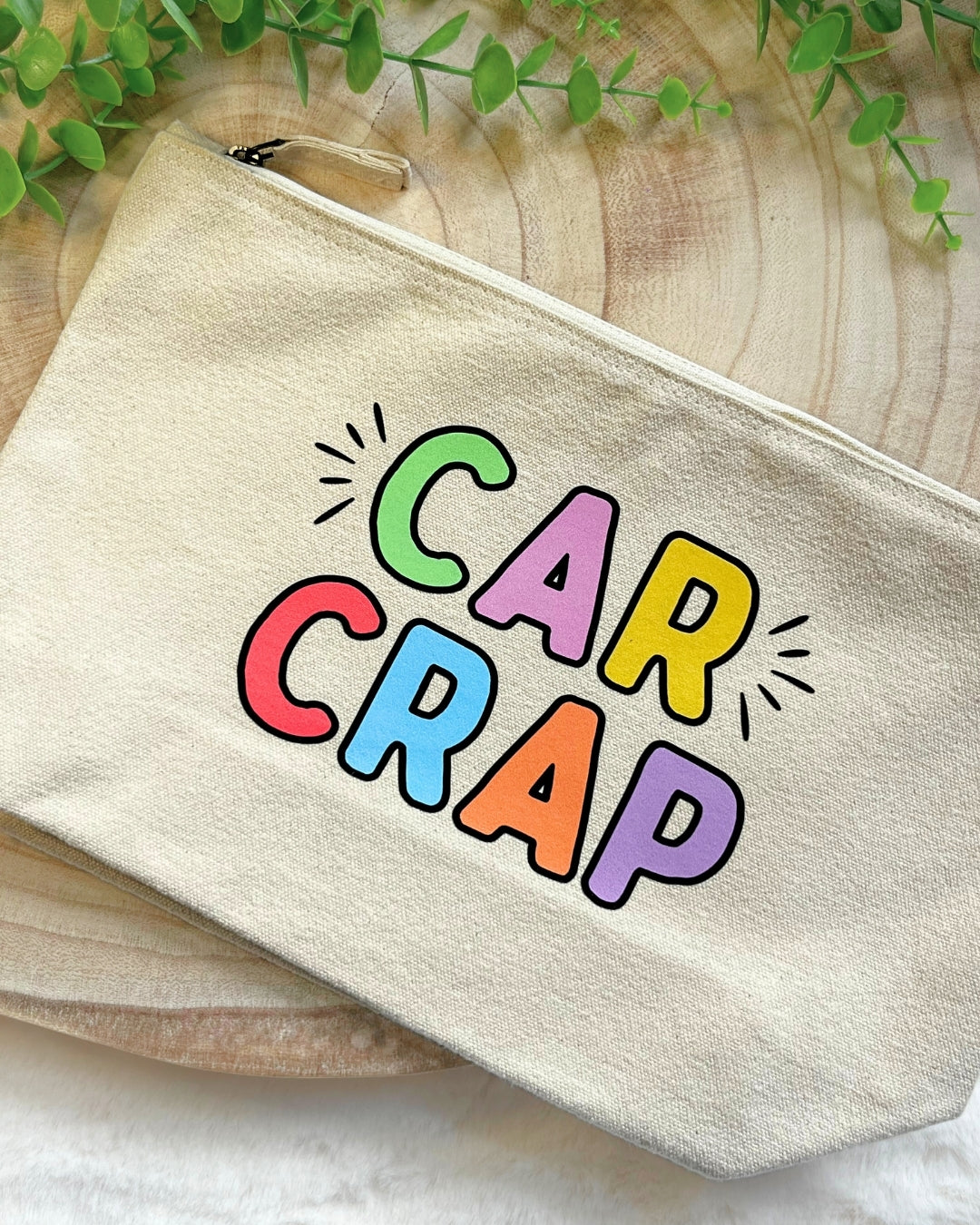 Cream canvas zip pouch with bold, colourful “Car Crap” lettering with a metal zipper
