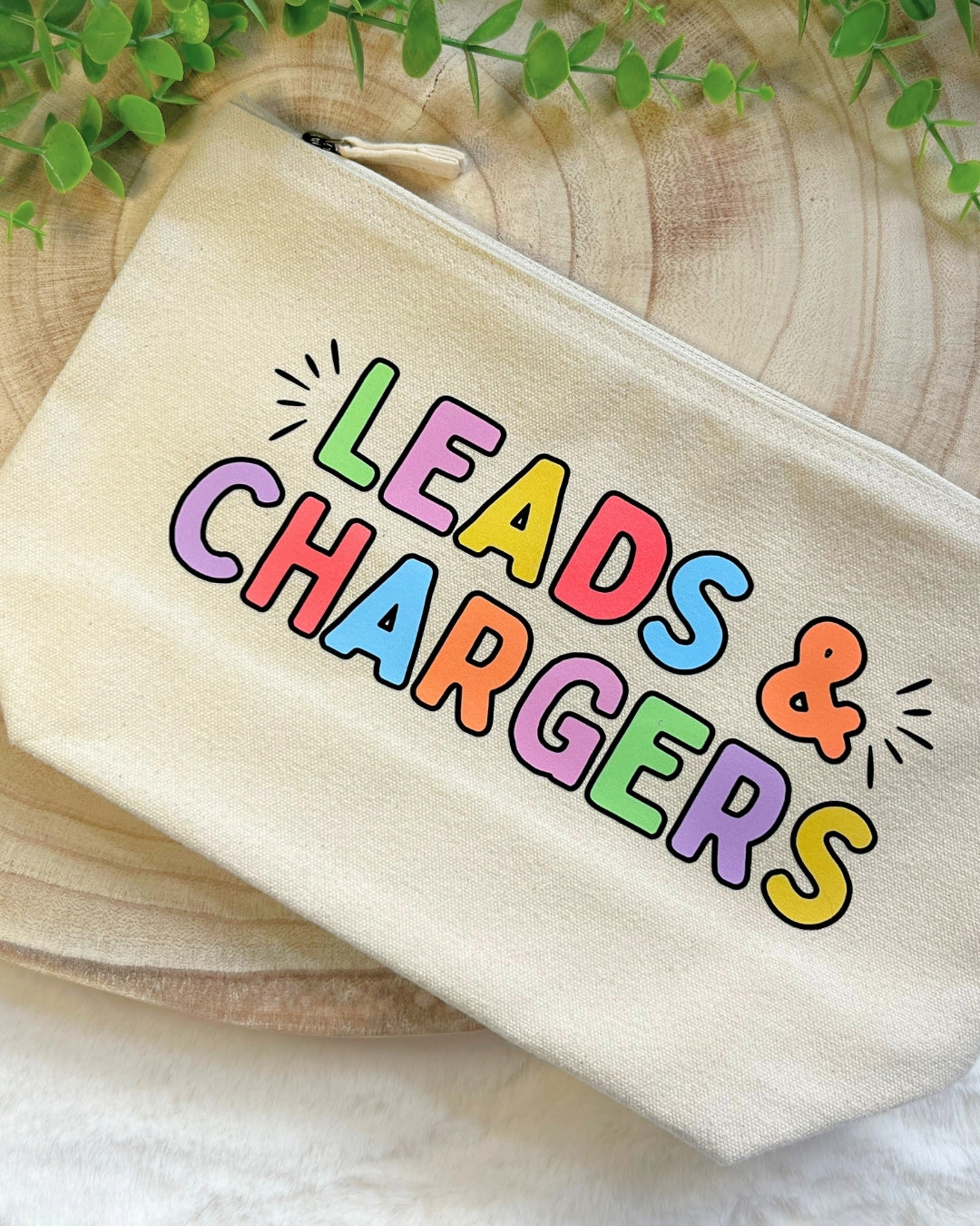 Cream coloured zip pouch with bold rainbow lettering “Leads & Chargers"