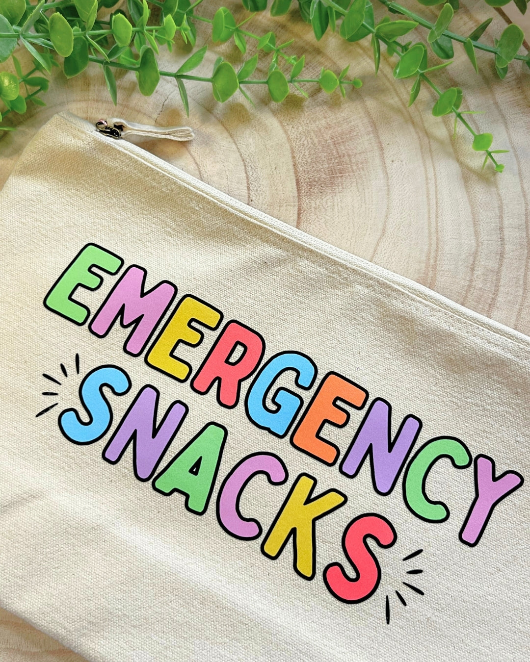 Cream coloured pouch with bold rainbow lettering “Emergency Snacks" with a metal zipper